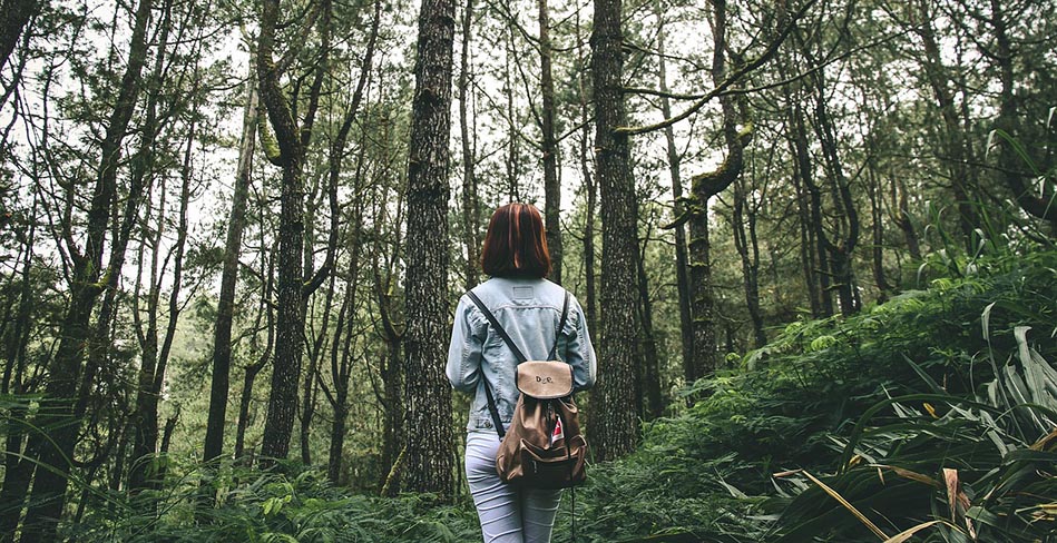 girl with backpack walking through forest